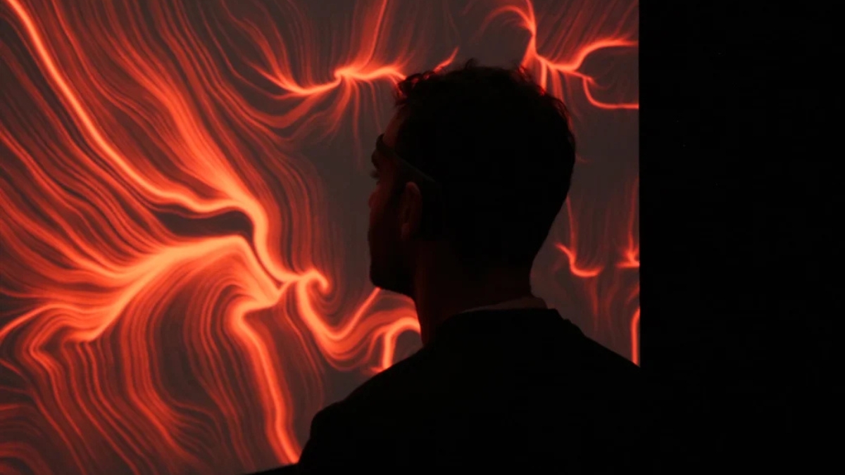 La silhouette di un uomo di profilo, con un sensore EEG, davanti a un grande schermo che mostra un'opera dalle linee e dai vortici rossi e arancioni su fondo nero.