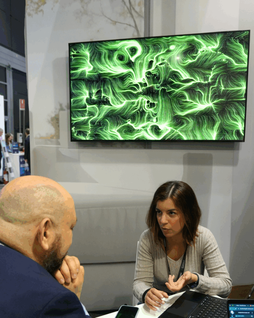 Due persone in conversazione a uno stand fieristico, con un quadro BrainArt® verde su uno schermo a parete alle loro spalle.