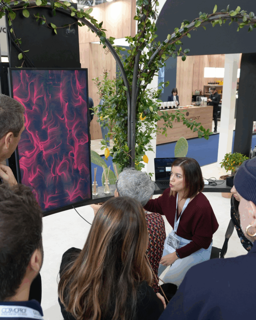 Una hostess presenta l'esperienza BrainArt® a un gruppo di visitatori a uno stand fieristico, accanto a uno schermo verticale con un quadro rosso.