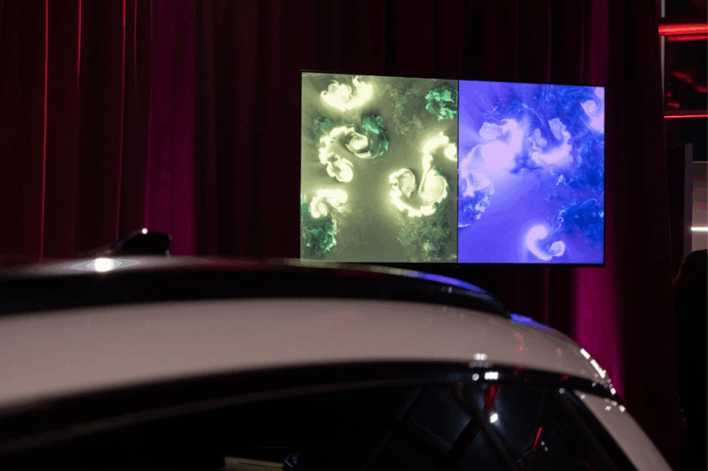Due quadri BrainArt®, uno verde e uno blu, su uno schermo dietro il profilo di un'auto chiara, davanti a tende di velluto rosso.