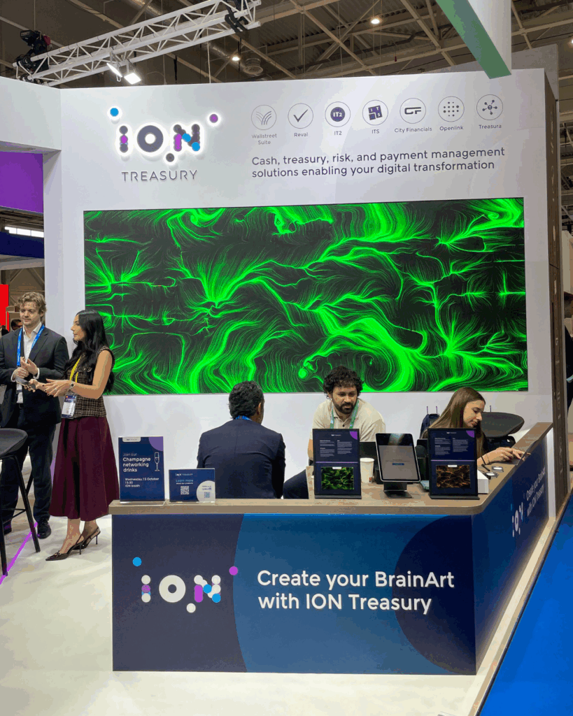 Stand fieristico con logo ION Treasury e un grande schermo che mostra un'opera dalle linee e dai vortici verdi su fondo nero; al bancone, con la scritta "Create your BrainArt with ION Treasury", alcune persone sedute davanti a tablet e altre in piedi accanto.