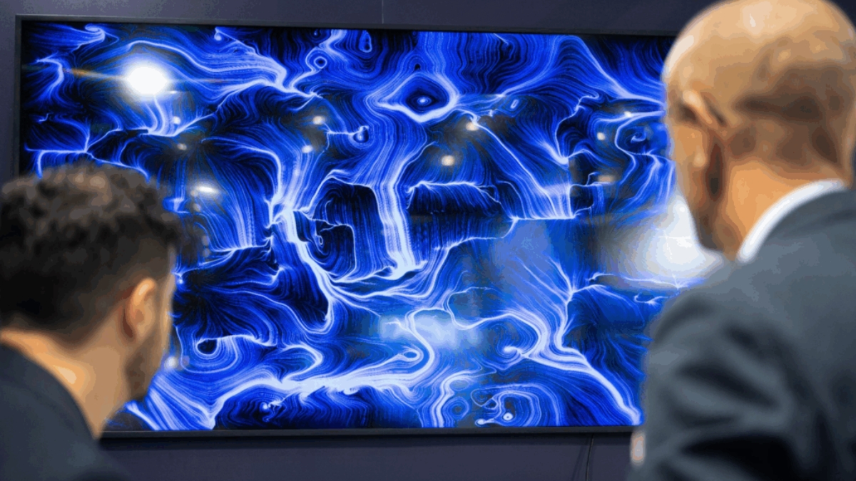 Due uomini di spalle osservano uno schermo appeso a parete che mostra un'opera dalle linee e dai vortici blu e bianchi su fondo scuro.