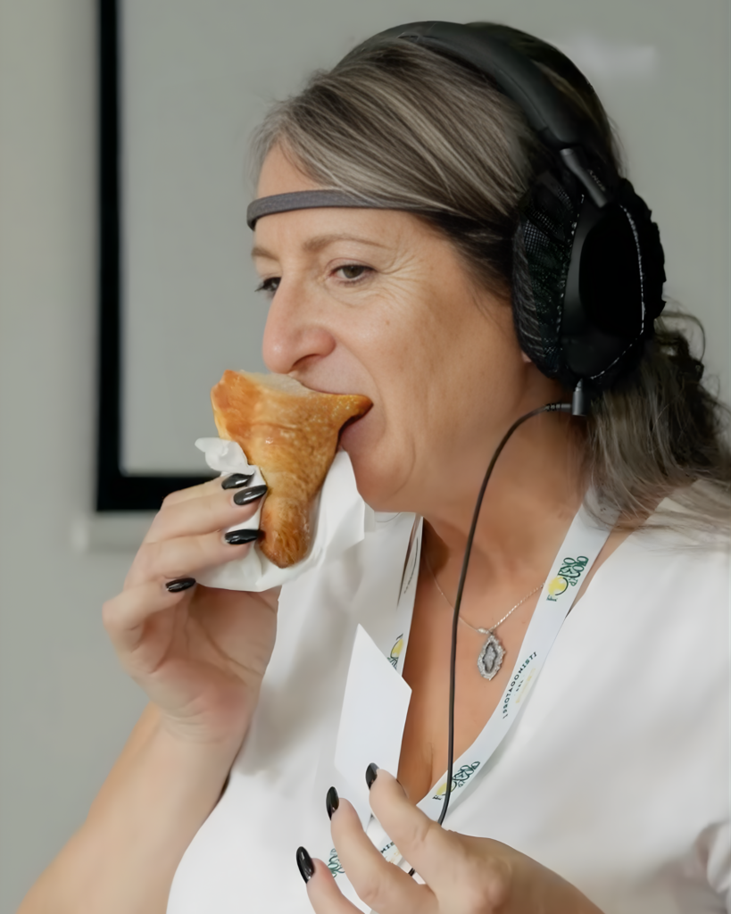 Una donna con un sensore EEG sulla fronte e le cuffie in testa dà un morso a un cornetto tenuto in un tovagliolo; indossa un pass al collo con il logo Forno d'Asolo.