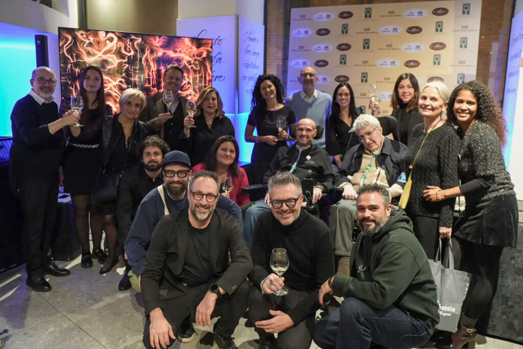 Gruppo di persone brinda con calici alzati a un evento serale in una piazza addobbata per Natale, con un operatore che riprende la scena