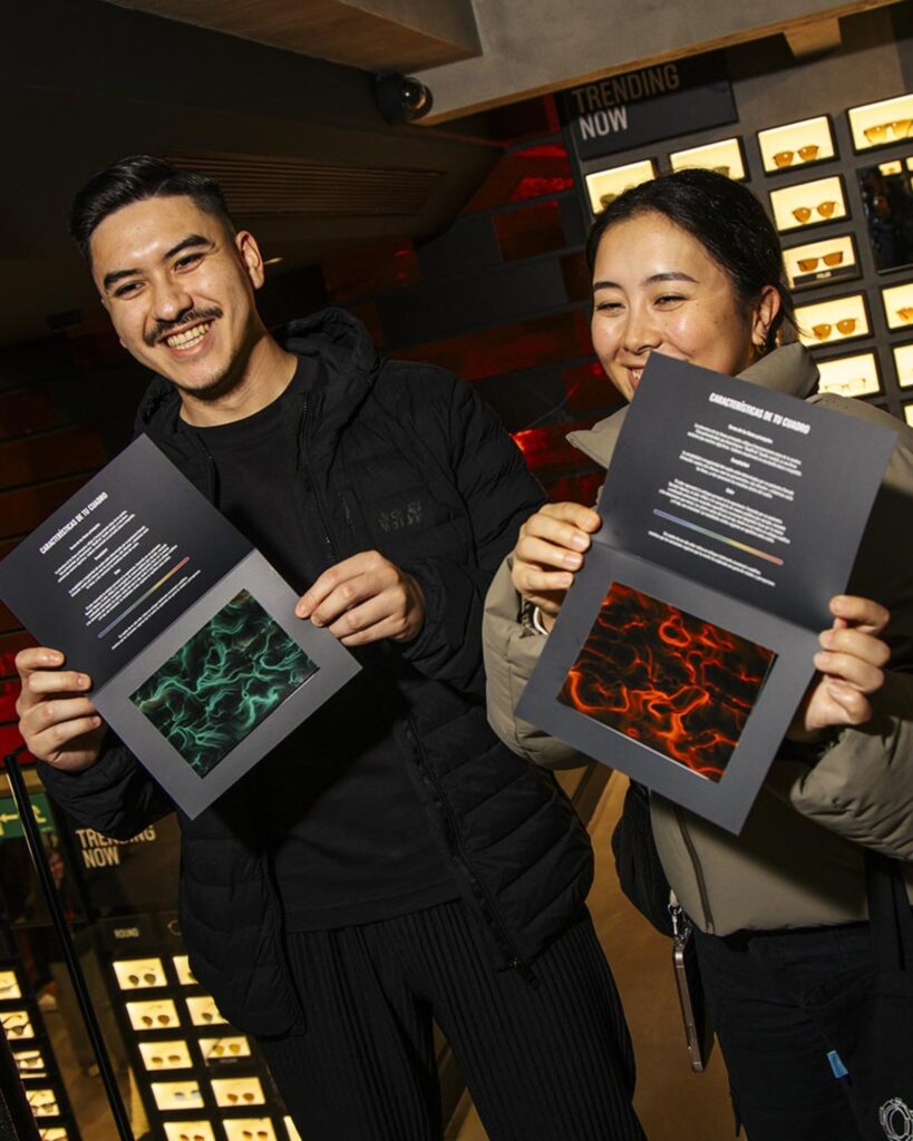 Un uomo e una donna sorridenti mostrano le stampe dei loro quadri BrainArt®, uno verde e uno rosso, in un negozio di occhiali da sole.