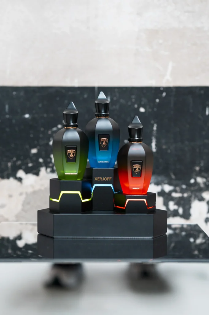 I tre flaconi delle fragranze Xerjoff x Automobili Lamborghini — Perseveranza verde, Avanguardia blu e Fierezza rossa  su un espositore nero con dettagli luminosi.