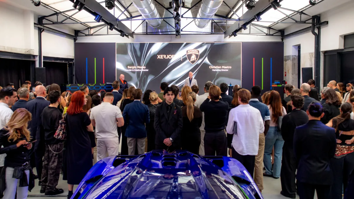 Sergio Momo e Christian Mastro sul palco durante il lancio della collezione Xerjoff x Automobili Lamborghini, davanti a un pubblico numeroso e a una supersportiva blu.