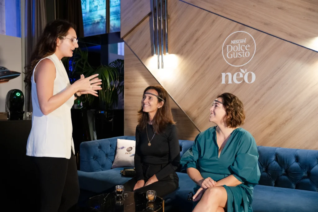 Una operatrice BrainArt presenta l'esperienza a due ospiti con il sensore EEG in fronte, al lancio di Nescafé Dolce Gusto NEO in Terrazza Duomo.