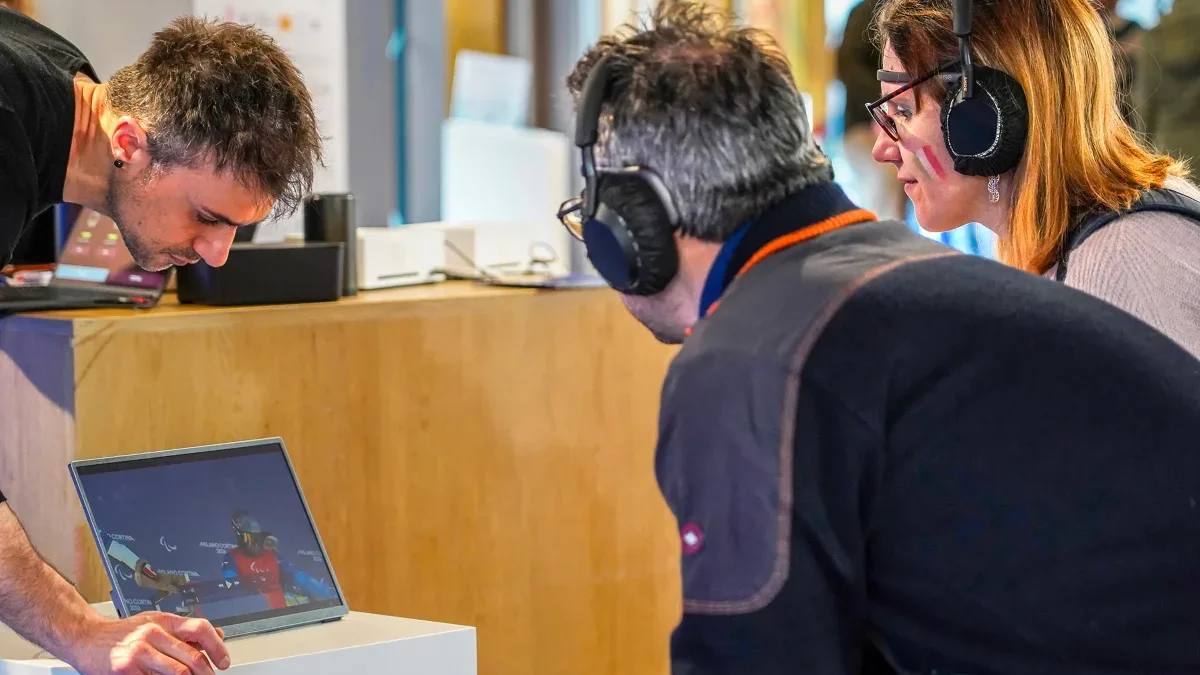 An operator checks the monitor while two participants wearing headphones watch the Milano Cortina Paralympics video