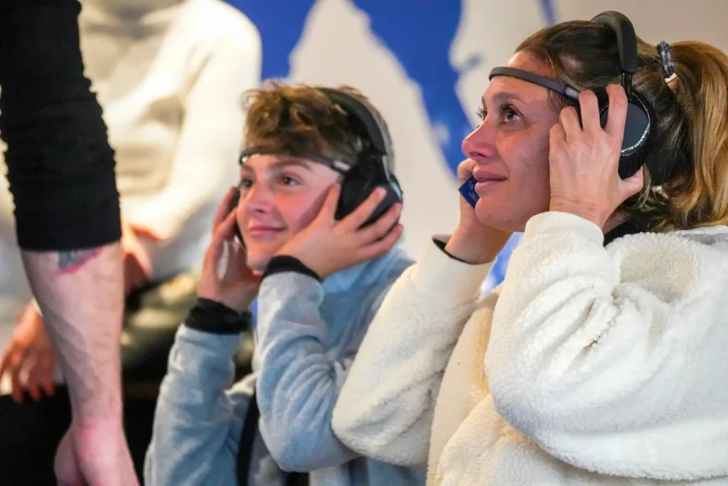 A woman and a boy wearing an EEG sensor and headphones smile as they watch the Paralympics video at the Ottobock event